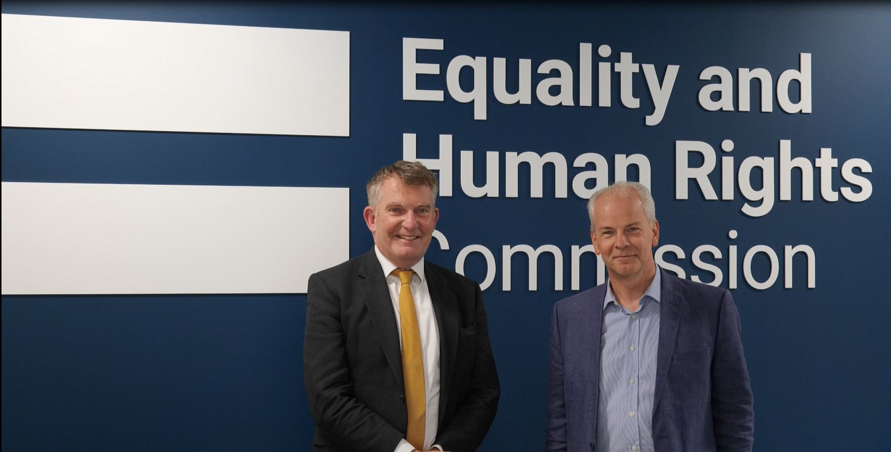 Marcial Boo and Nigel Ellis from LGSCO stand in front of a wall with the Equality and Human Rights Commission on it