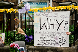 Floral tributes for the Grenfell Tower fire, with a large banner that says 'Why?'