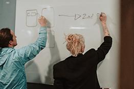 A man and woman write on a whiteboard
